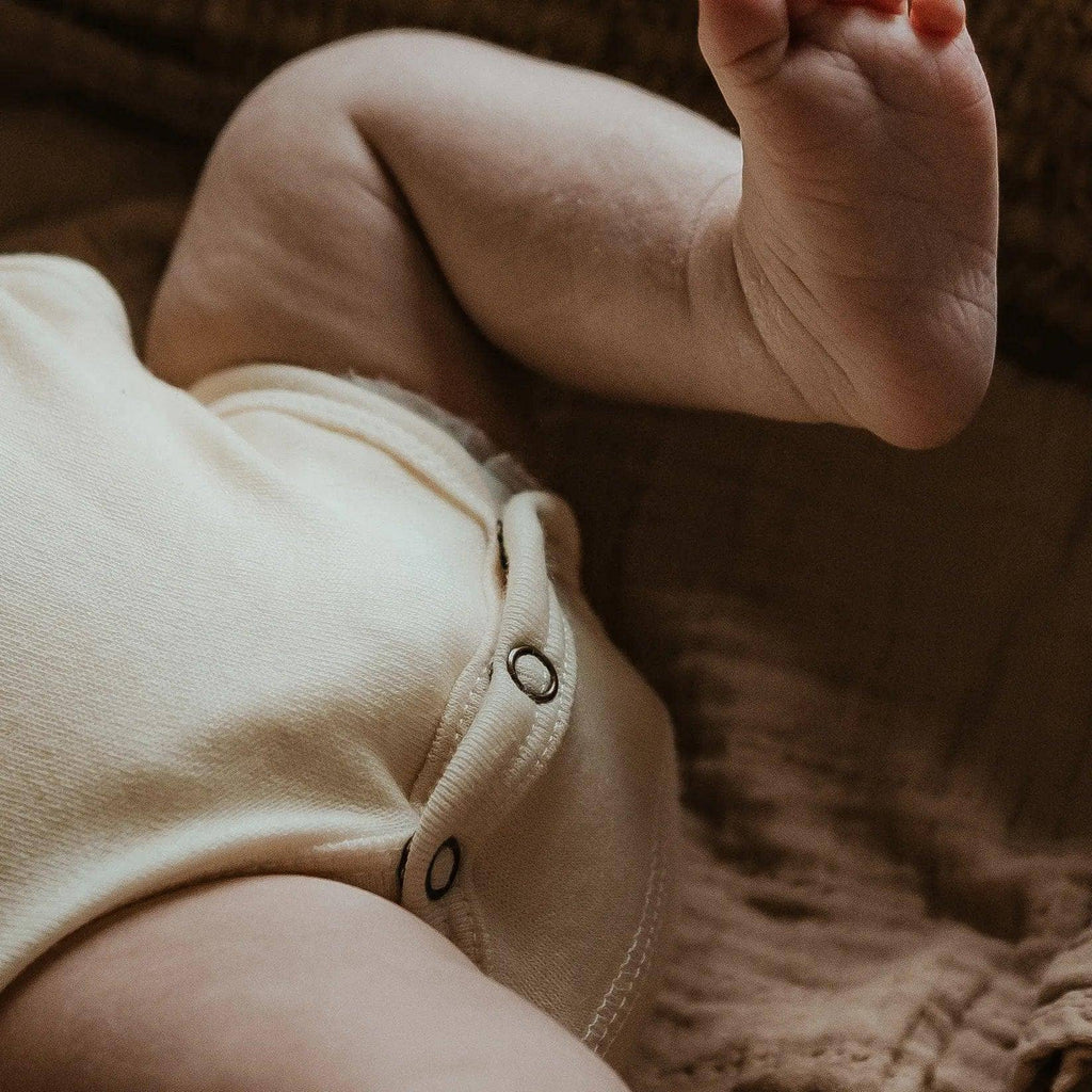 Bébé portant un body en laine mérinos naturelle non traitée, doux pour la peau et adapté à la régulation thermique. détail sur les pressions de l'entre jambe Couleur : Naturel