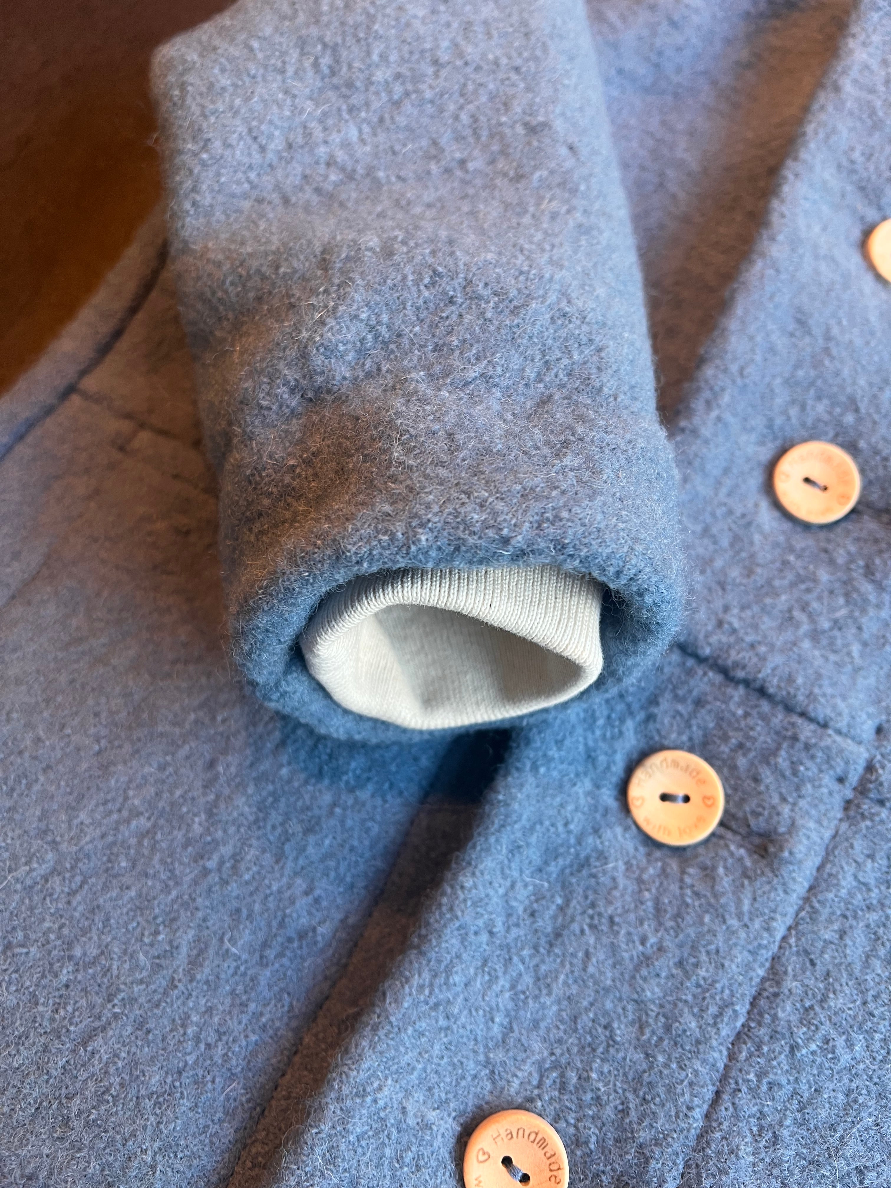 Gros plan sur le poignet d'un manteau enfant en laine, montrant la texture naturelle de la maille et la précision des coutures.