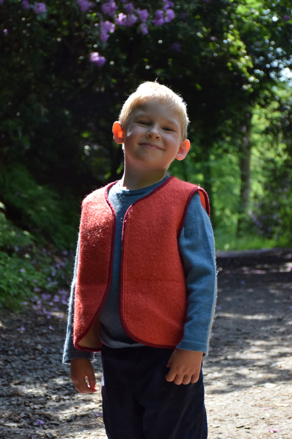 Enfant portant un  gilet sans manche en laine upcycler de couleur rouge. vue de trois quart