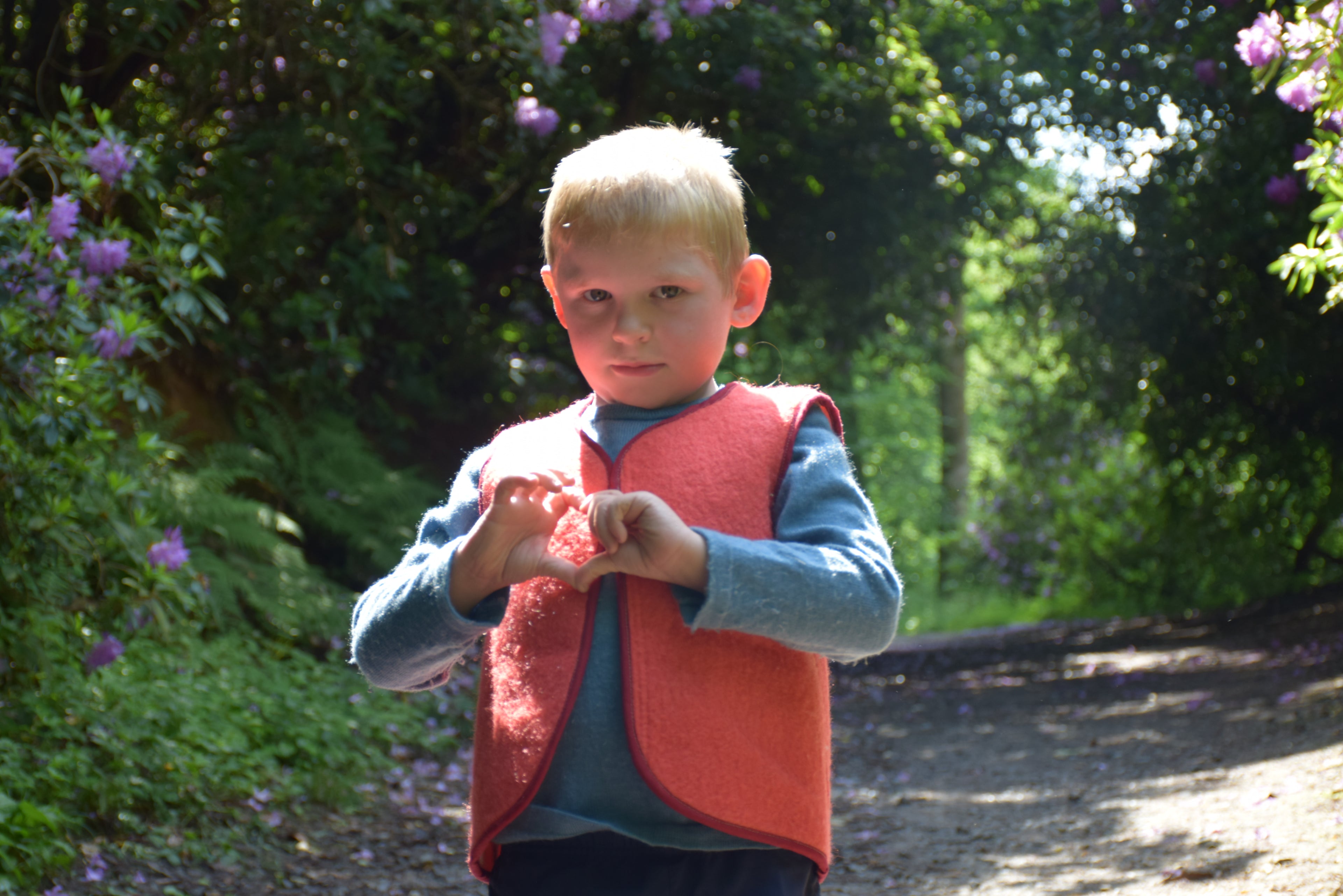 Enfant portant un  gilet sans manches en laine upcyclée de couleur rouge. vue de face. l'enfant fait un coeur vec ses doigts