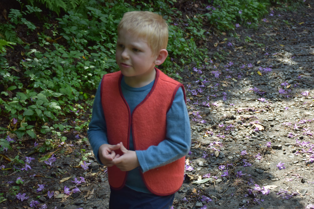 Enfant portant un  gilet sans manches en laine upcyclée de couleur rouge. vue de côté