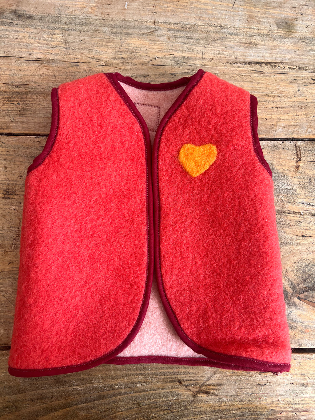 gilet sans manche en laine upcycler de couleur rouge avec un coeur orange sur la poitrine du côté gauche