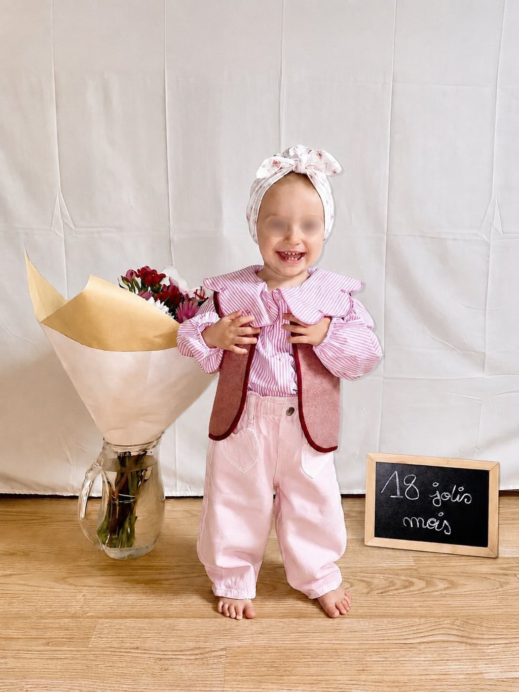 enfant portant un gilet sans manche en laine upcycler de couleur vieux-rose avec un coeur rouge sur la poitrine du côté gauche. l'enfant est de face