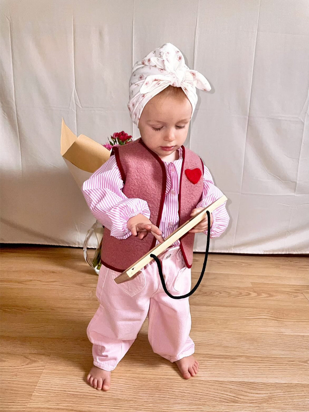 enfant portant un gilet sans manche en laine upcycler de couleur vieux-roseavec un coeur rouge sur la poitrine du côté gauche. l'enfant a un jouet en main