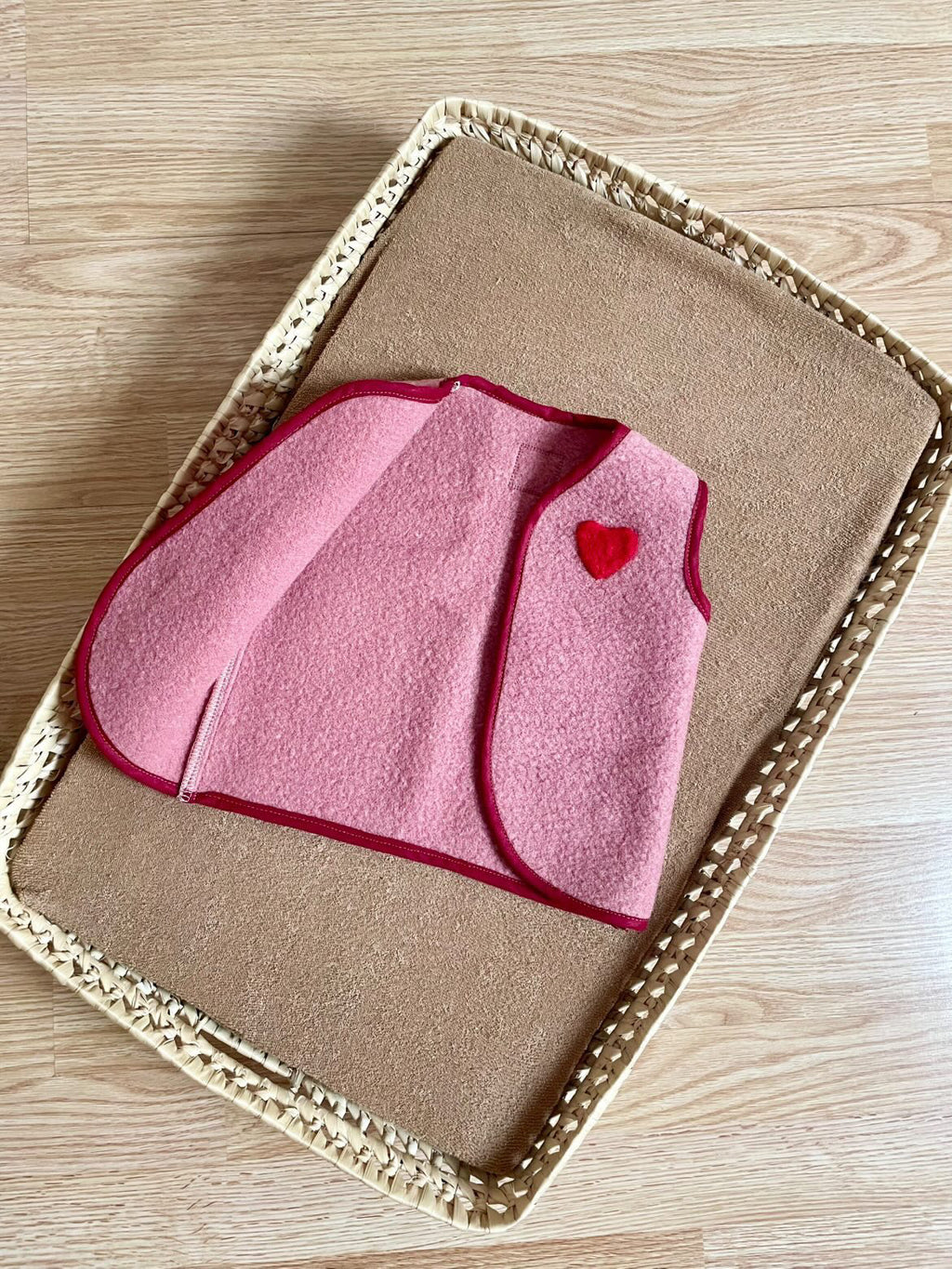 gilet sans manche en laine upcycler de couleur vieux-rose avec un coeur rouge sur la poitrine du côté gauche. le gilet est présenté ouvert d'un côté