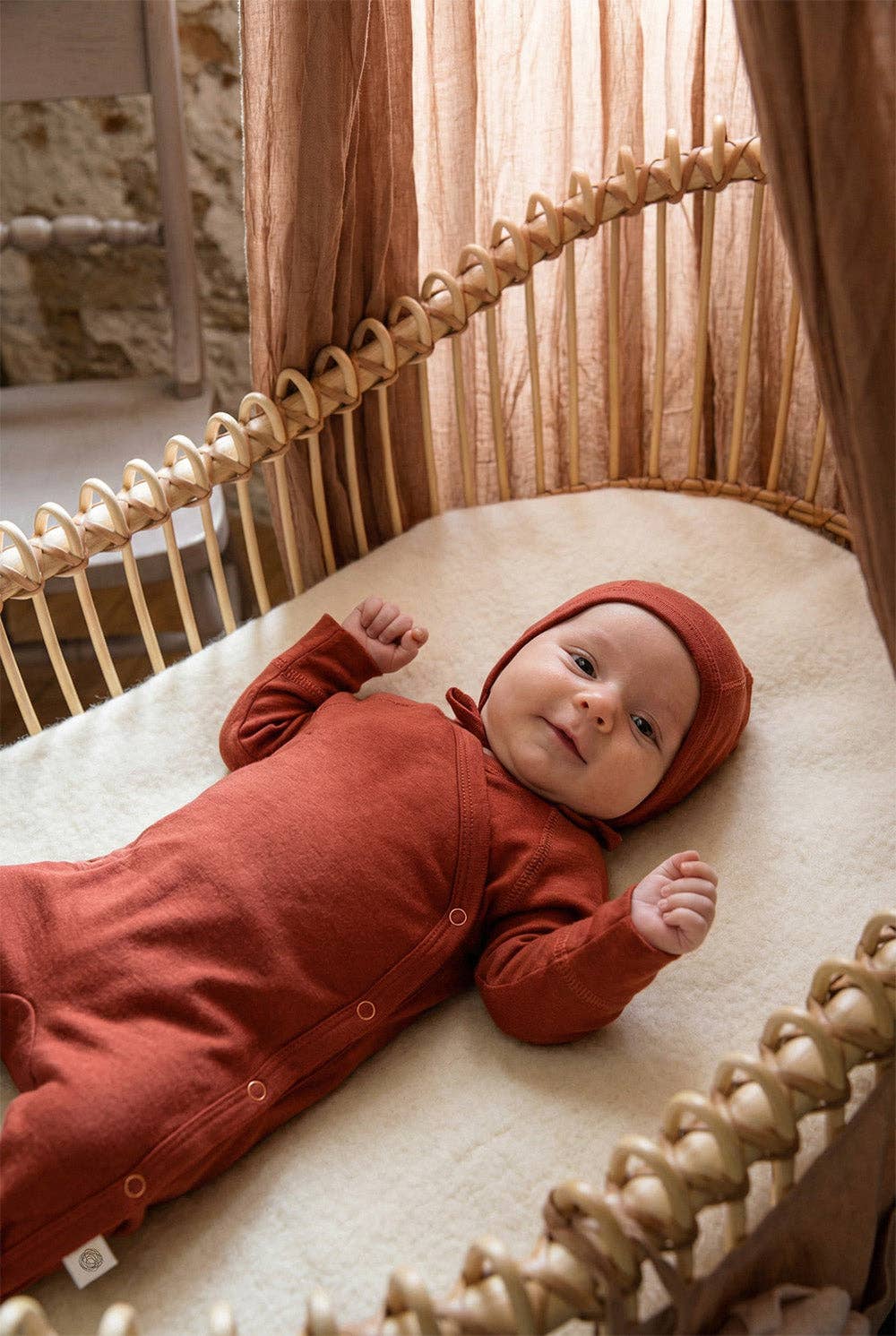 Bébé couché portant une combinaison en laine mérinos non traitée, idéale pour protéger du froid tout en laissant respirer la peau Couleur : Henné