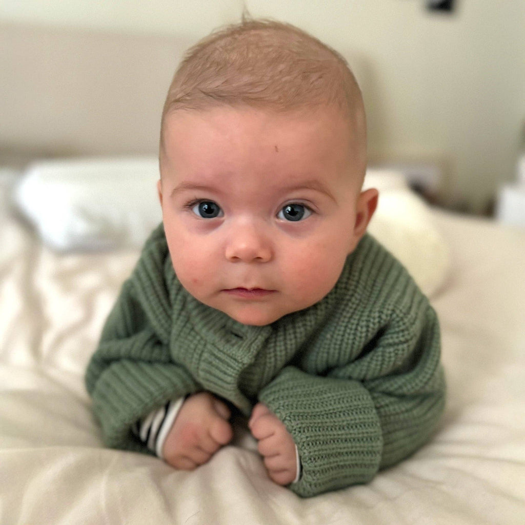 Bébé couché sur le ventre portant un cardigan en laine mérinos naturelle non traitée, couche chaude et respirante couleur verte