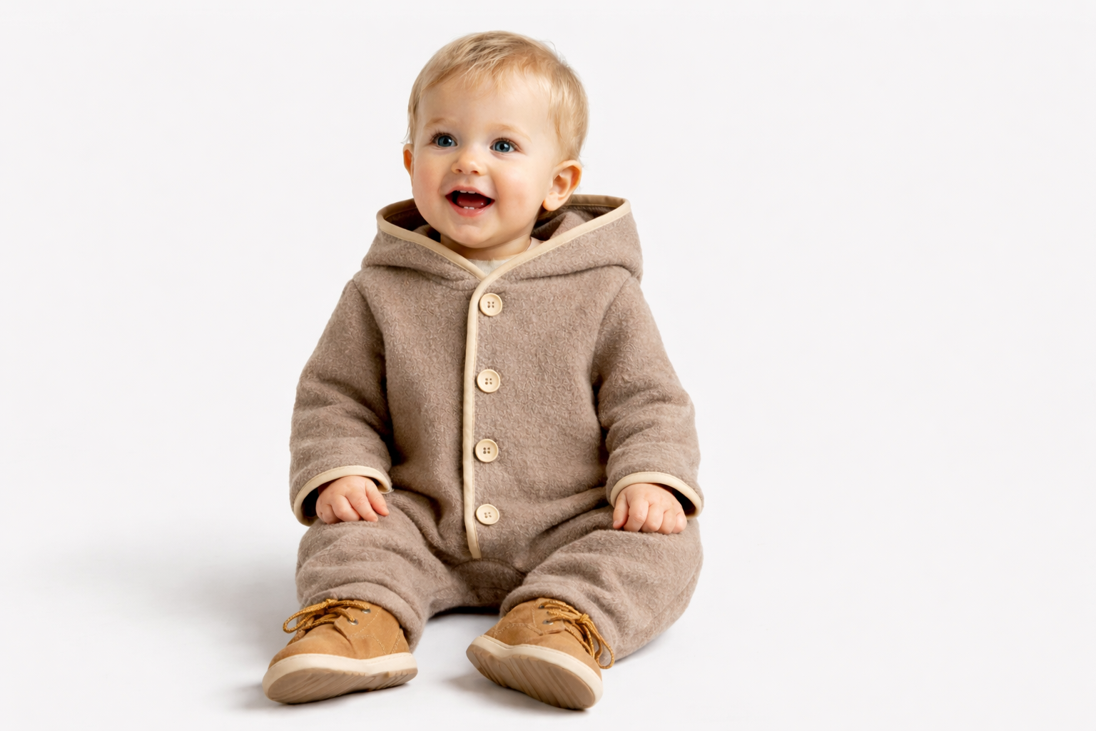 Combinaison pilote à capuche en laine mérinos de couleur beige, vue de face sur un cintre. Elle est dotée d'une fermeture avant avec des boutons en bois et d'un liseré bleu foncé contrastant le long des bords de la capuche, de la patte de boutonnage, des manches et des pieds intégrés